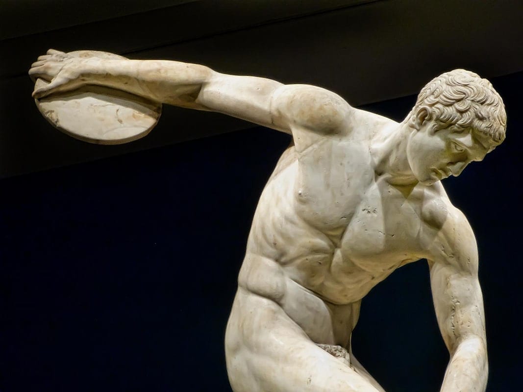  A marble statue of a muscular young man throwing a discus, with a dark background.
